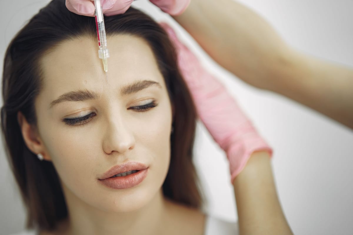 A gloved clinician giving a cosmetic injection to a patient's forehead
