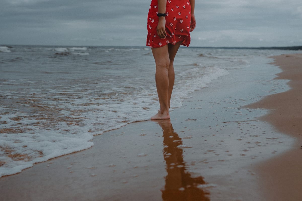 Bare legs walking at the water's edge on a sandy beach